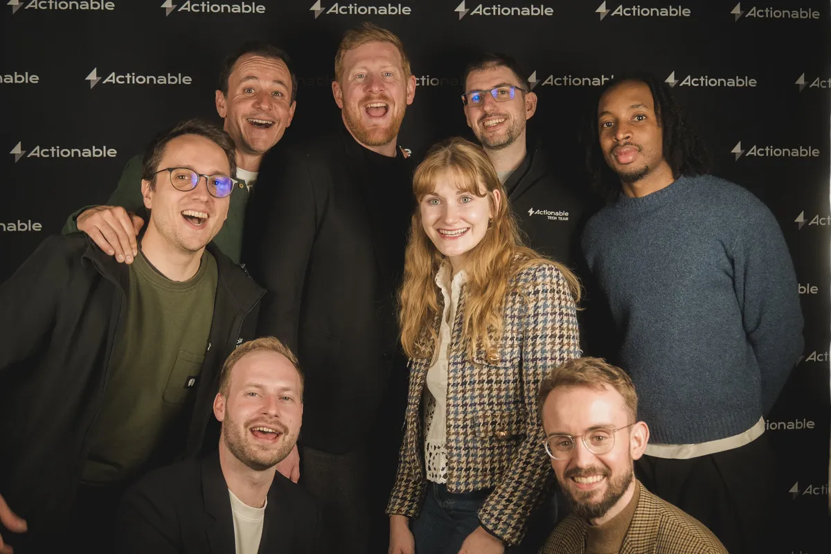 Actionable team photo, everyone smiling in front of the Actionable photo wall